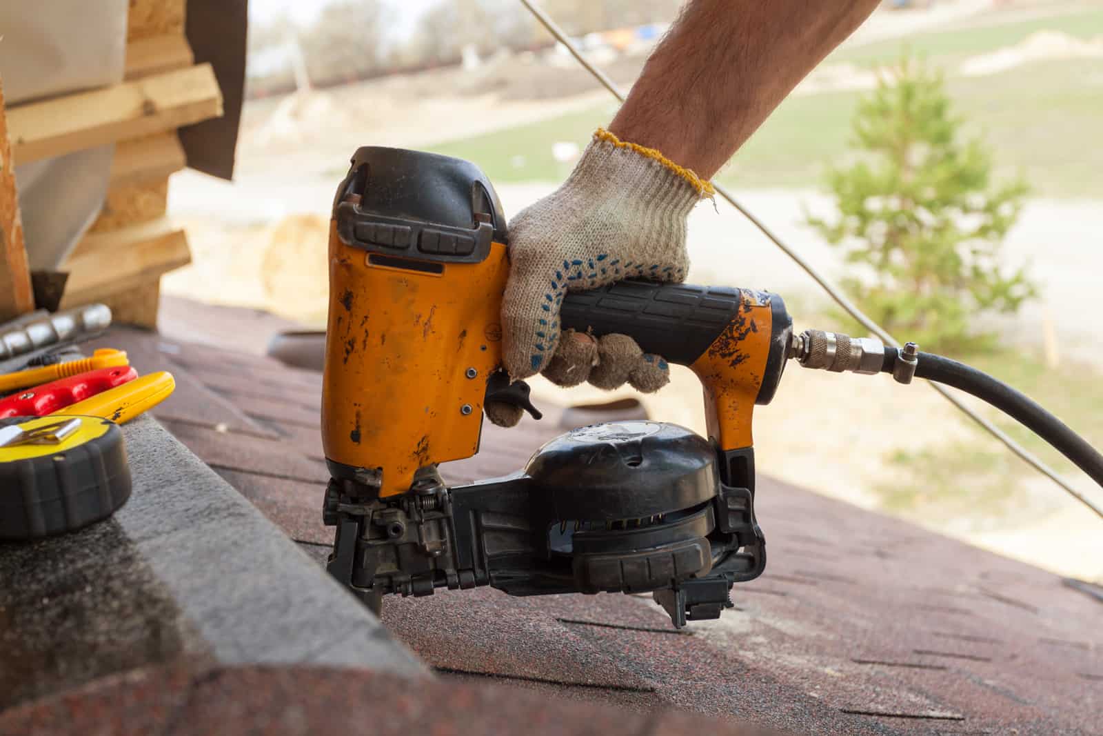 roofer using nail gun to install asphalt shingles